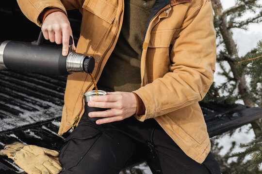 Man sitting on truck tailgate pouring hot coffee from a thermos