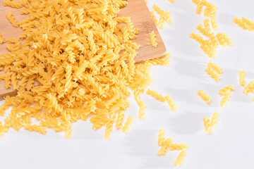 Uncooked Fusilli Pasta Scattered on Wooden Board and White Table. Raw and Dry Macaroni. Fat and Unhealthy Food