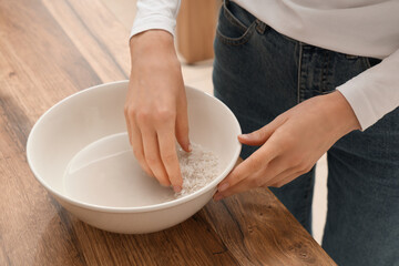 Woman rinsing rice in bowl near wooden table, closeup