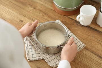 Woman holding pot with water and rice near table in kitchen, closeup