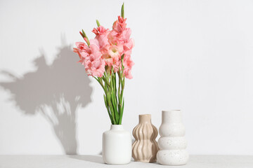 Vase with bouquet of beautiful gladiolus flowers on table against white background