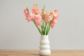 Vase with bouquet of beautiful gladiolus flowers on wooden table against white background