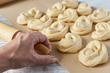 A woman's hand holding a rolling pin against a background of dough buns on a baking sheet. Cooking...