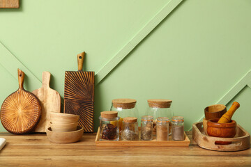 Jars with spices and utensils on counter near green wall in kitchen