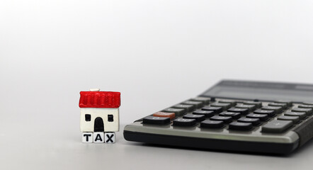 Housing model and calculator with alphabet TAX on white background. Business investment and property tax concept.
