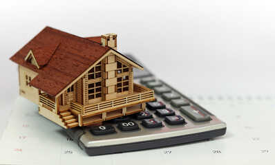 A calculator and a wooden house are placed on the calendar. Business investment and real estate...