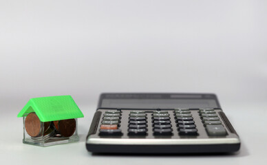 A house with coins and a calculator are placed on a white background. Business, finance, and budget...