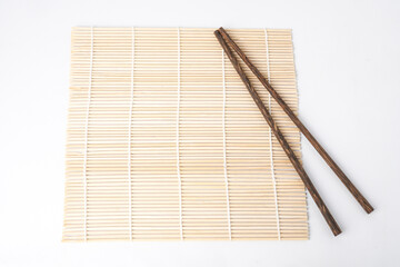 Close-up photo of Japanese wooden chopsticks laid on woven bamboo mat or makisu. Isolated over white background. Shot on flat lay high angle setup.