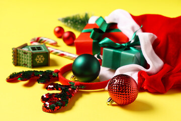 Santa bag with Christmas decorations, gift boxes, candy cane and reindeer horns on yellow background