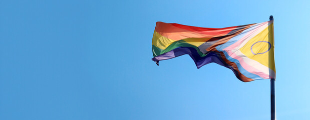 Intersex-inclusive redesign of the Progress Pride Flag. Rainbow LGBT flag against a blue sky. Flag...