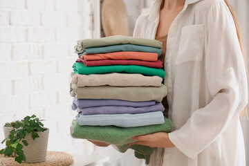 Young woman with stack of stylish clothes at home, closeup