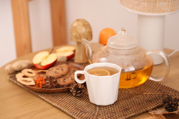 Teapot, cup of green tea, plate with cookies and autumn decor on table in room. Closeup