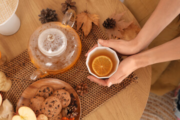 Female hands with cup of green tea near plate with food and autumn decor on table in room. Closeup