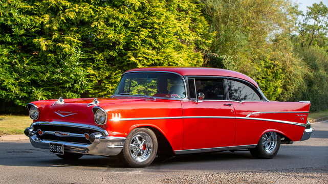 1957 red Chevrolet Bel Air American car driving on a British country road.