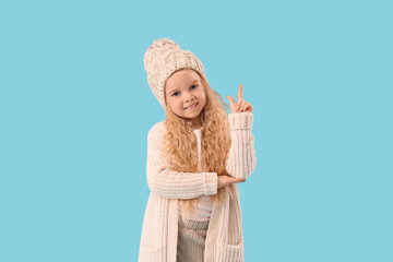 Cute little girl in winter clothes pointing at something on blue background