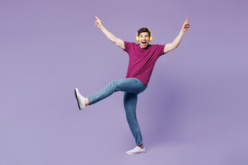 Full body young happy man he wear violet t-shirt casual clothes listen to music in headphones raise...