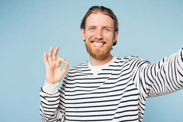 Fototapeta premium Close up young happy man he wear striped sweatshirt casual clothes doing selfie shot pov on mobile cell phone show ok okay isolated on plain pastel light blue cyan background studio Lifestyle concept