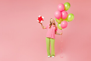 Full body young woman wears shirt celebrating birthday holiday and hold bunch of colorful air balloons hold present box with gift ribbon bow isolated on plain light pink background. Lifestyle concept.