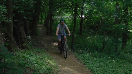 A man cyclist riding on a path in a green forest on a sunny summer day.