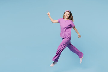 Obraz premium Full body side view calm smiling young woman wear purple pyjamas jam sleep eye mask rest relax at home jump high run fast hurry up isolated on plain blue cyan background. Good mood night nap concept.
