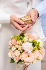 Wedding photo, details of the hands of the bride and groom holding a case with wedding rings and a wedding bouquet of delicate flowers