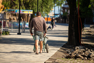 A man is walking down a sidewalk with a wheelbarrow