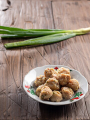 A plate of steamed Indonesian siomay served without sauce, set on a rustic wooden table. Fresh green onions are placed in the background, creating a simple yet appetizing display.