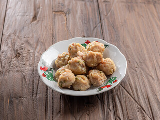 A plate of steamed Indonesian siomay arranged neatly on a decorative dish with a rooster design. The plate is set on a rustic wooden table, offering a simple and appetizing presentation of the dish.