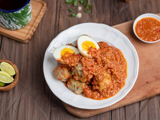 A plate of traditional siomai, a type of Indonesian steamed dumpling served with a spicy peanut sauce and accompanied by hard-boiled eggs. a hand holding a fork is lifting a piece