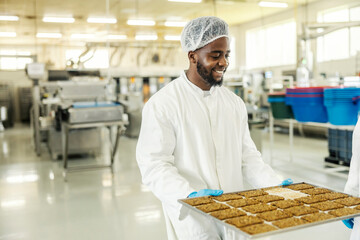 Happy diverse food factory worker carrying tray with fresh baked biscuits.