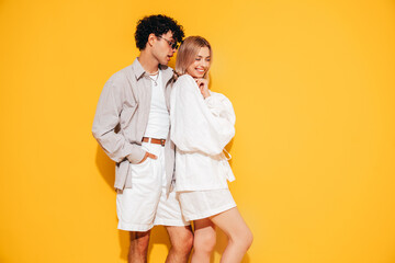 Happy beautiful romantic teenage couple. Smiling handsome caucasian man and young woman in summer clothes posing in studio, hugging sharing emotions, cheerful and happy. Isolated on yellow, sunglasses