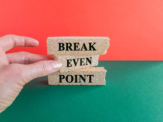 Break even point symbol. Concept words Break even point on brick blocks on a beautiful green table, red background. Businessman hand. Business and BEP break even point concept.