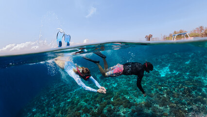 A young woman and a man snorkel underwater with a mask and fins in the ocean together. They dive...