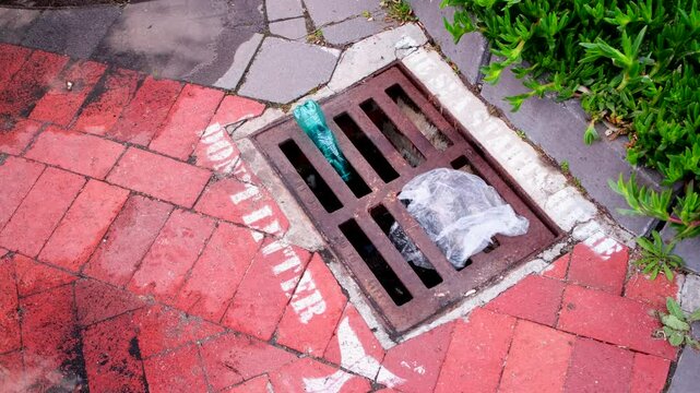 Ironic view of plastic refuse stuck in storm water drainage grate on coastline with stencils warning people to not litter because the ocean starts there