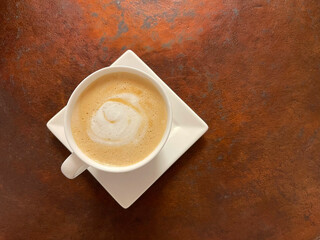 A cup of cappuccino on a rough, aged metal background