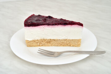 Piece of homemade cheesecake and small dessert fork on the white plate. Close-up. 