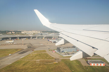 The plane is taking off. View from the window to the wing of the aircraft, runway, airfield and sky.