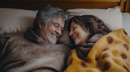 A joyful couple in their sixties share a light-hearted moment in bed, wrapped in a cozy blanket