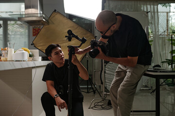 Assistant helping cameraman to set equipment before footage