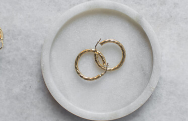 Overhead view of gold hoop earrings on a marble tray, top view of solid gold earrings on a marble...