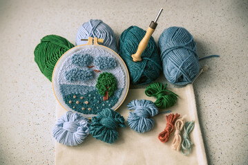 Woolen embroidery in blue colors together with balls of yarn and a punch needle.