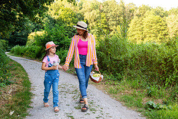 Fototapeta premium Mother and her daughter are walking together in a forest park. Woman and a girl are going on a family picnic.