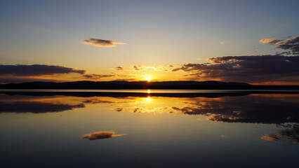 Sunset on the lake with a mirror image of the sun and sky on the water. Landscape view of the lake, calm environment. Beauty is in nature.