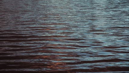 Sunlight plays on the calm sea waves. The surface of the sea water at sunset. Ripples on the water in close-up.