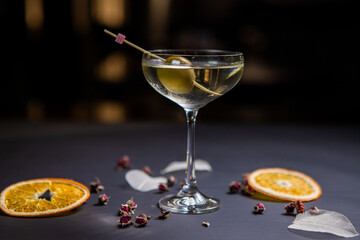 Martini cocktail decorated with an olive in a glass on a thin stem, on a table decorated with dried oranges
