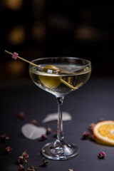 Martini cocktail decorated with an olive in a glass on a thin stem, on a table decorated with dried...