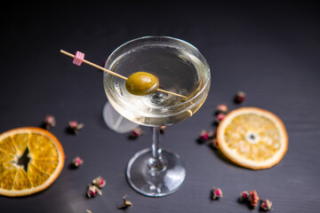 Martini cocktail decorated with an olive in a glass on a thin stem, on a table decorated with dried...