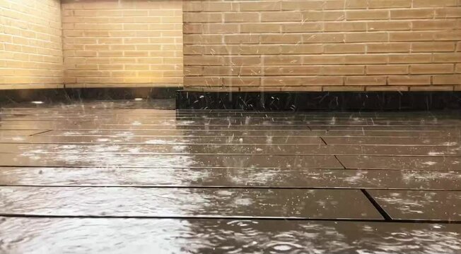 V&iacute;deo de las gotas de lluvia golpeando el suelo. Gotas de lluvia rebotando en el suelo moderno de tablones de madera de un patio con paredes de ladrillo.