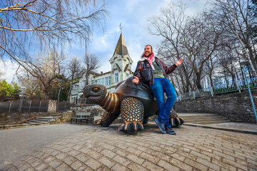 Tourist enjoys playful moment on a turtle statue in a park in Latvia on a bright, clear day