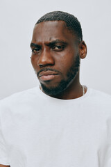 Obraz premium Portrait of a confident black man with a serious expression, wearing a white t shirt, set against a soft gray background, conveying strength and individuality